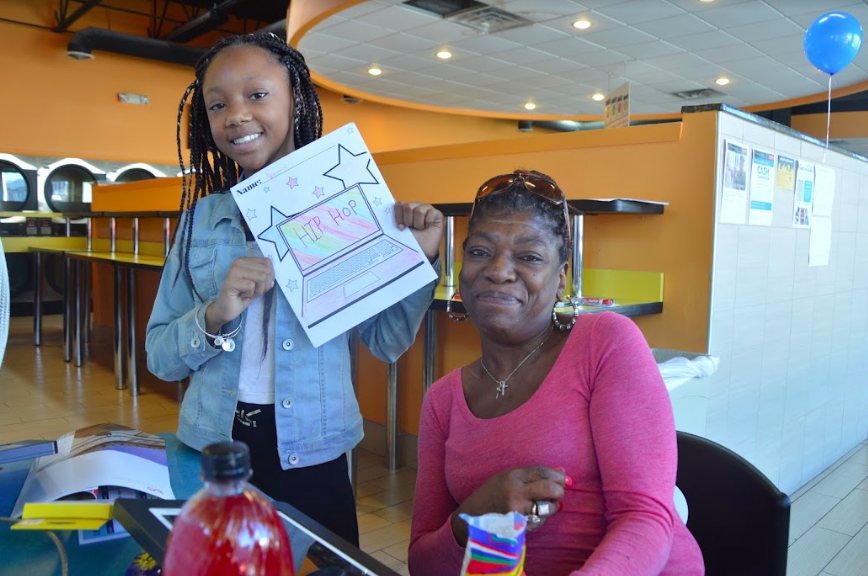 B Wali Digital Inclusion Week photo featuring a woman and young girl holding a picture of a laptop that she has colored in